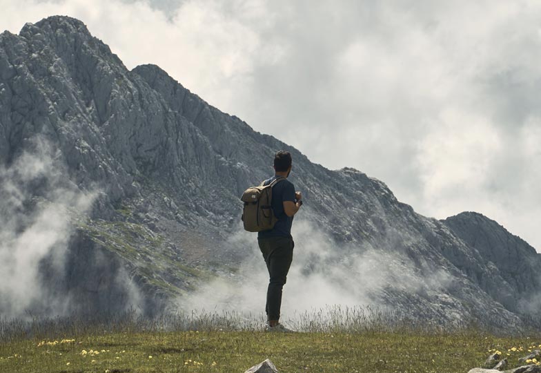 Homme de dos debout face à une montagne majestueuse, tenant une tasse, incarnant la prise de recul et la reconnexion à soi, au cœur de l'expérience Rando Formation.