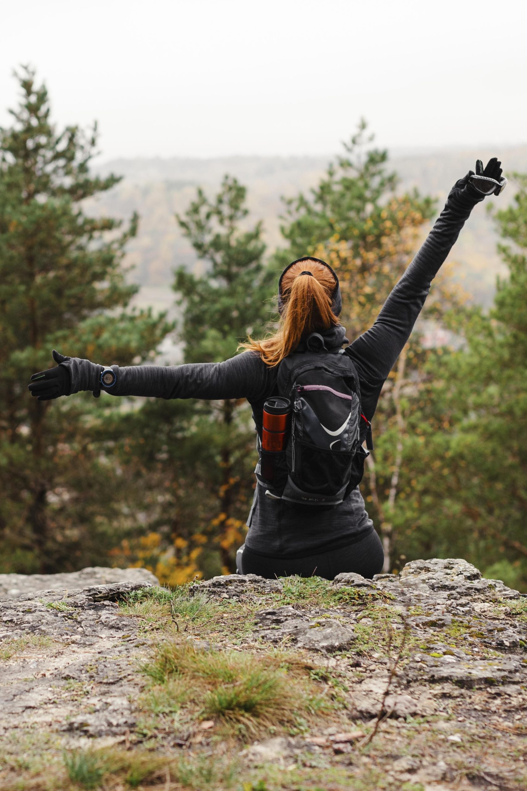 Femme de dos, assise sur un rocher en pleine forêt, bras ouverts vers le ciel – symbole de libération mentale et d’ancrage dans la nature, au cœur de la Rando Formation.